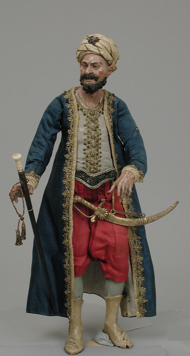 King's attendant, Giuseppe Gori, Polychromed terracotta head and wooden limbs; body of wire wrapped in tow; cotton and satin garments with silver and gold metallic thread; velvet belt backed with leather; brass sword; wooden and ivory staff; glass stones on turban