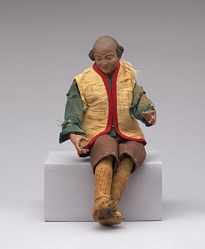 Man in beige vest with red trim, blue shirt, knee-length brown trousers