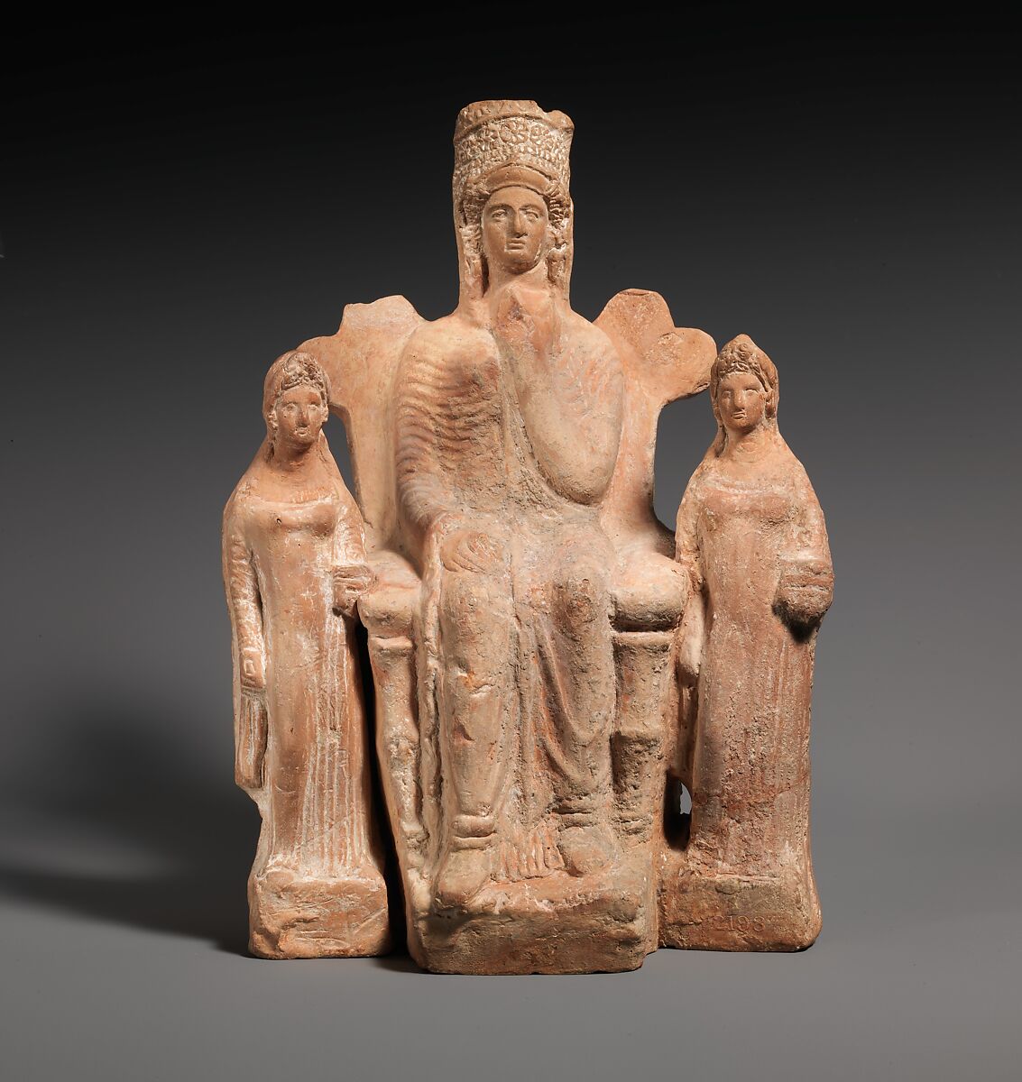 Terracotta statuette of an enthroned goddess between two attendants ...