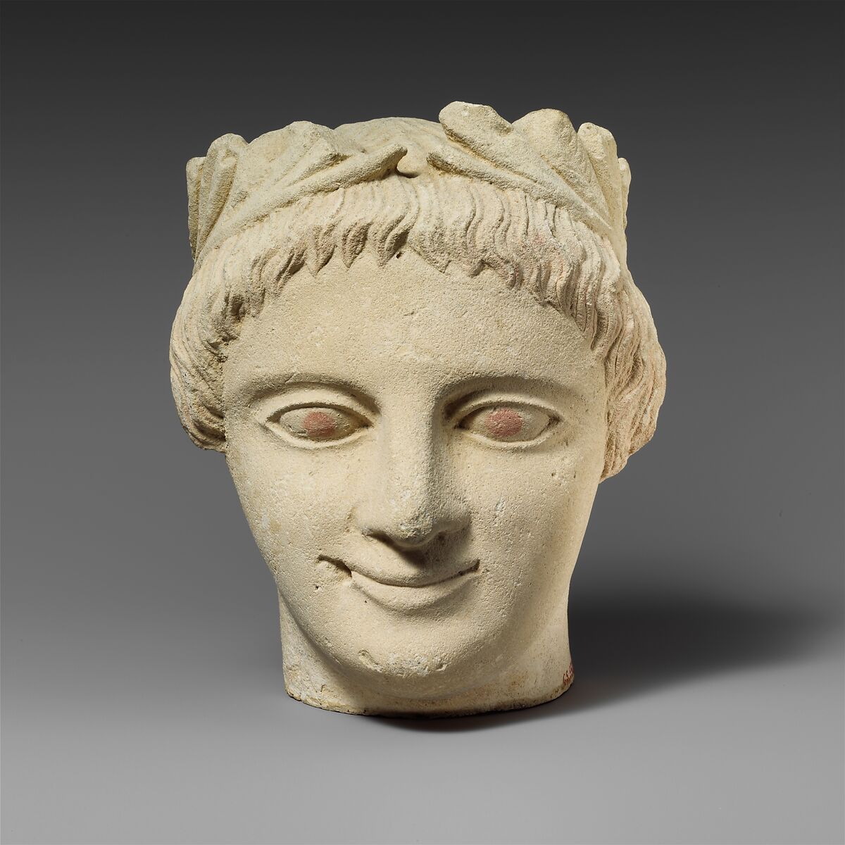 Limestone head of a beardless male votary with a wreath of leaves, Limestone, Cypriot 