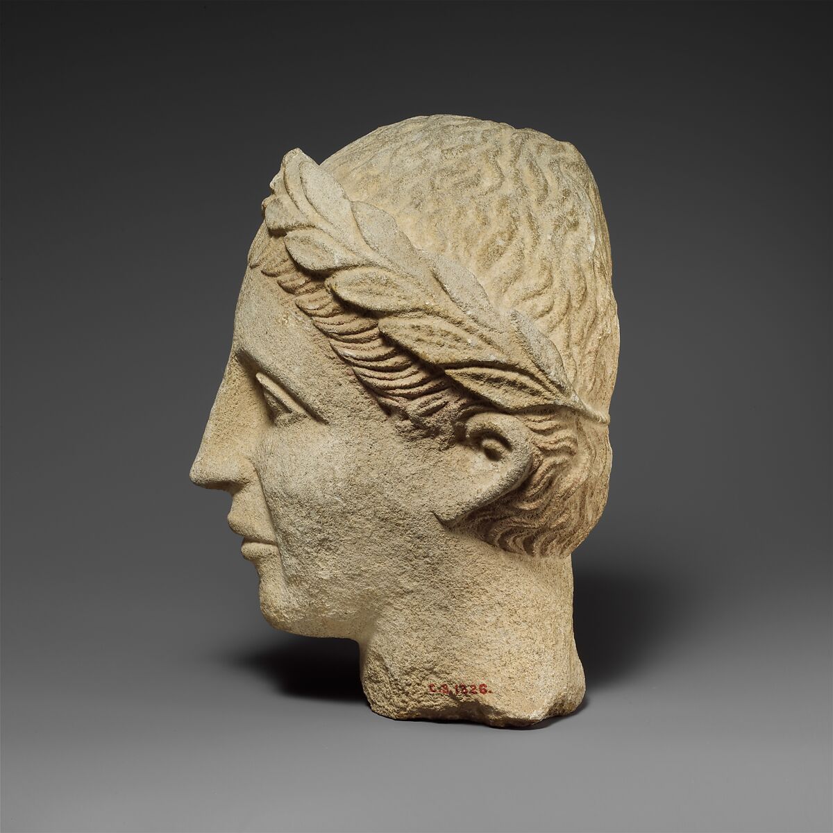 Limestone head of a beardless male votary with a wreath of leaves, Hard limestone, Cypriot