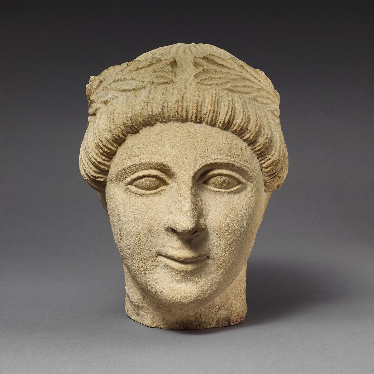 Limestone head of a beardless male votary with a wreath of leaves, Limestone, Cypriot 