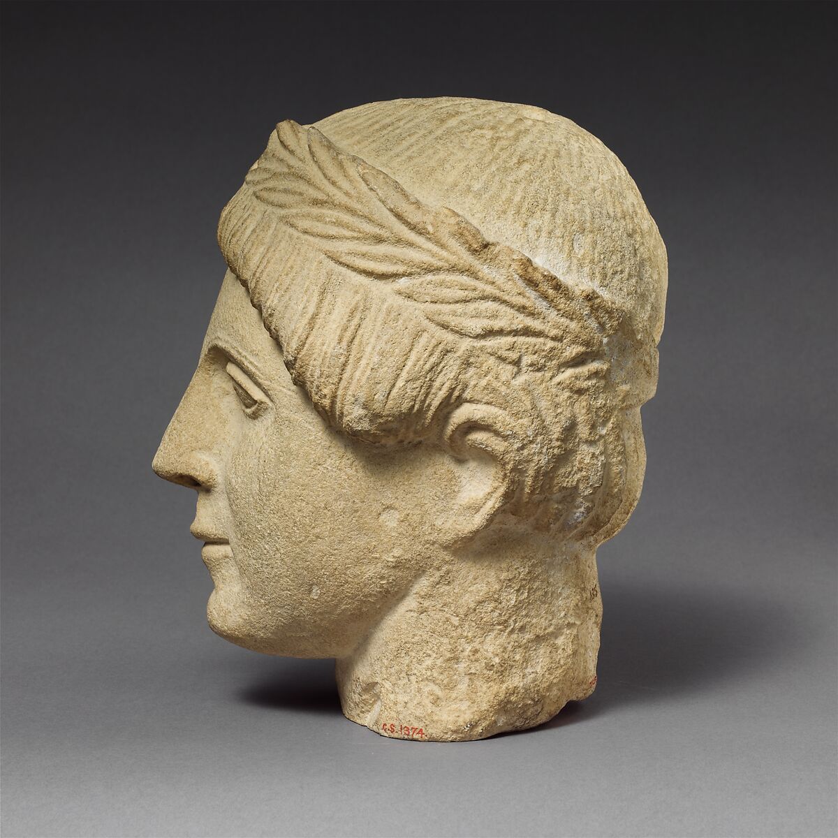 Limestone head of a beardless male votary with a wreath of leaves, Limestone, Cypriot