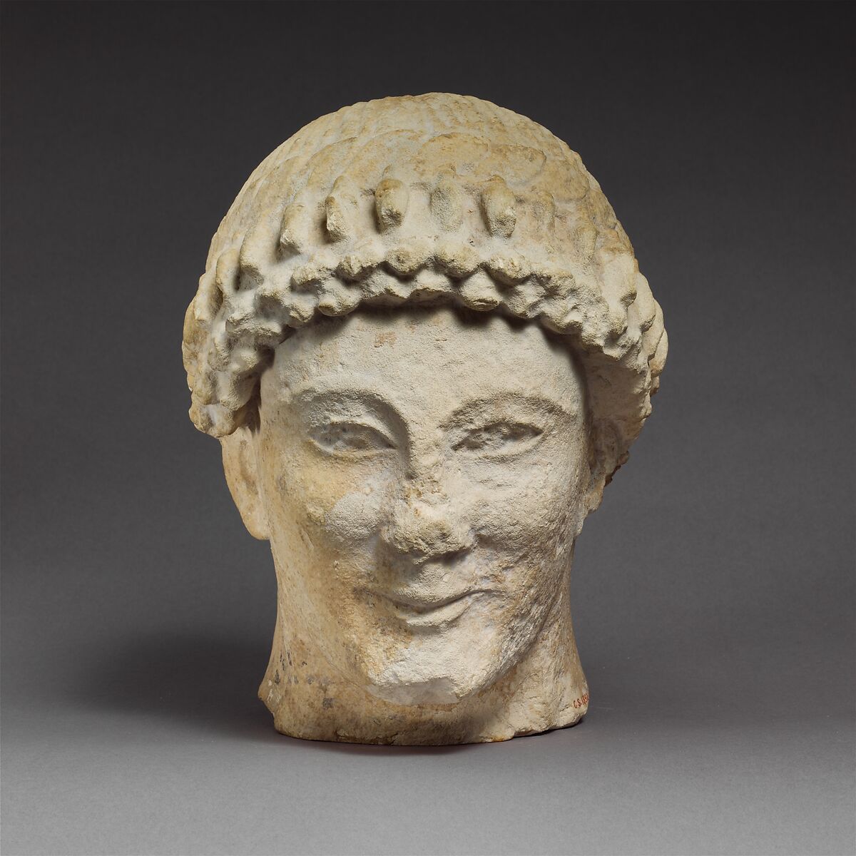 Limestone head of a beardless male with a wreath of flower buds ...