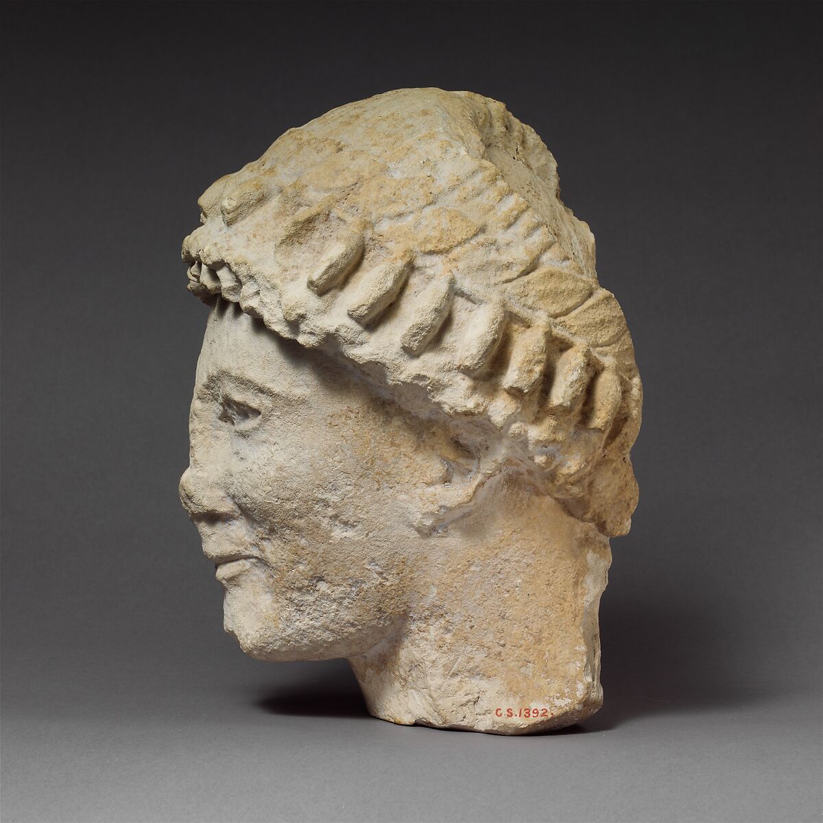 Limestone head of a beardless male with a wreath of flower buds, Limestone, Cypriot