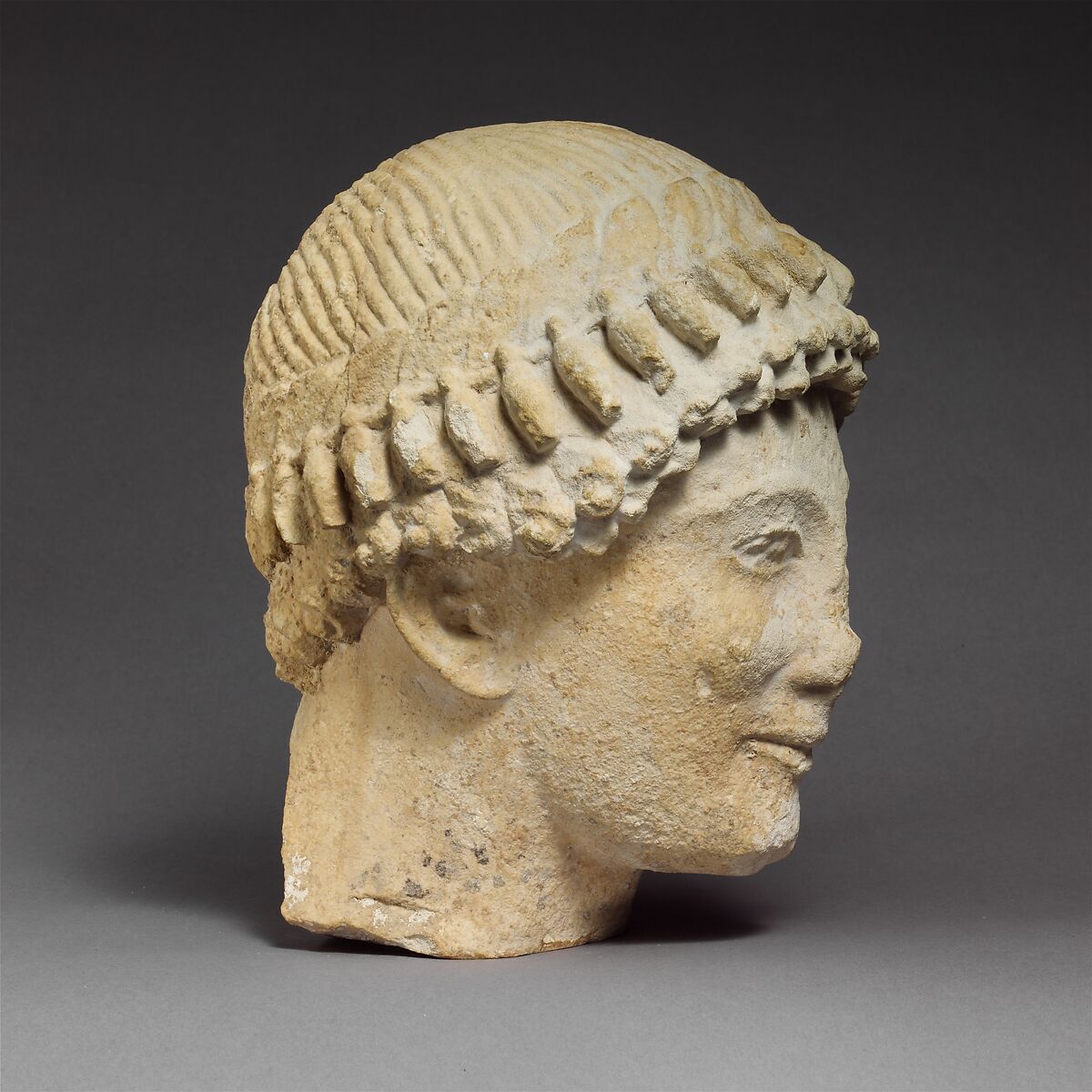 Limestone head of a beardless male with a wreath of flower buds, Limestone, Cypriot