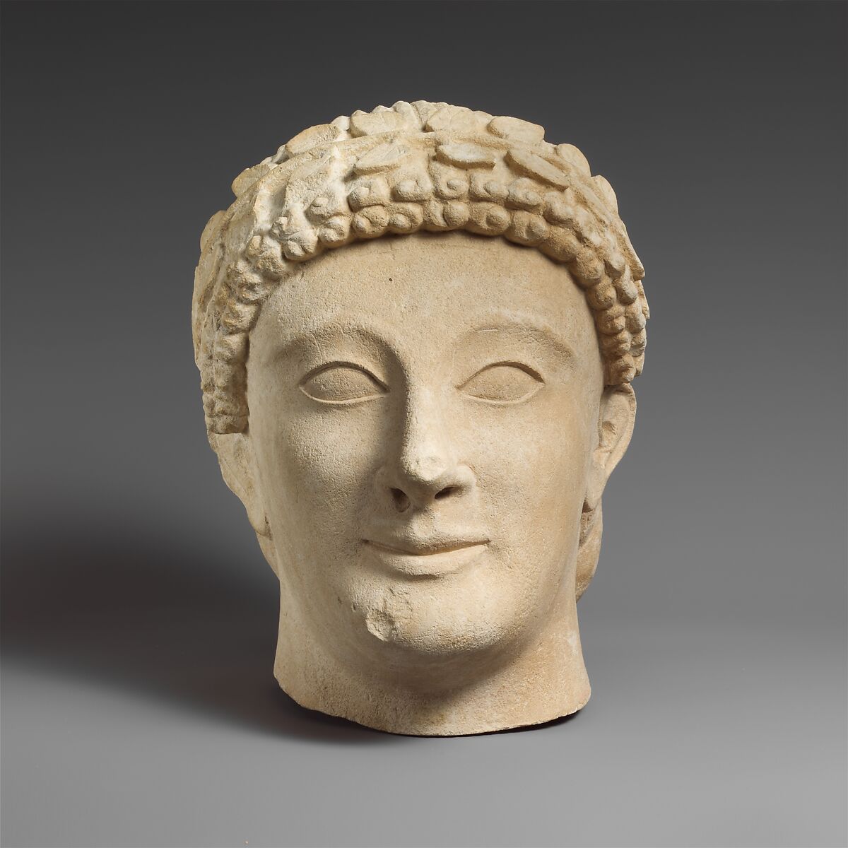 Limestone head of a beardless male votary with a wreath of leaves, Limestone, Cypriot 