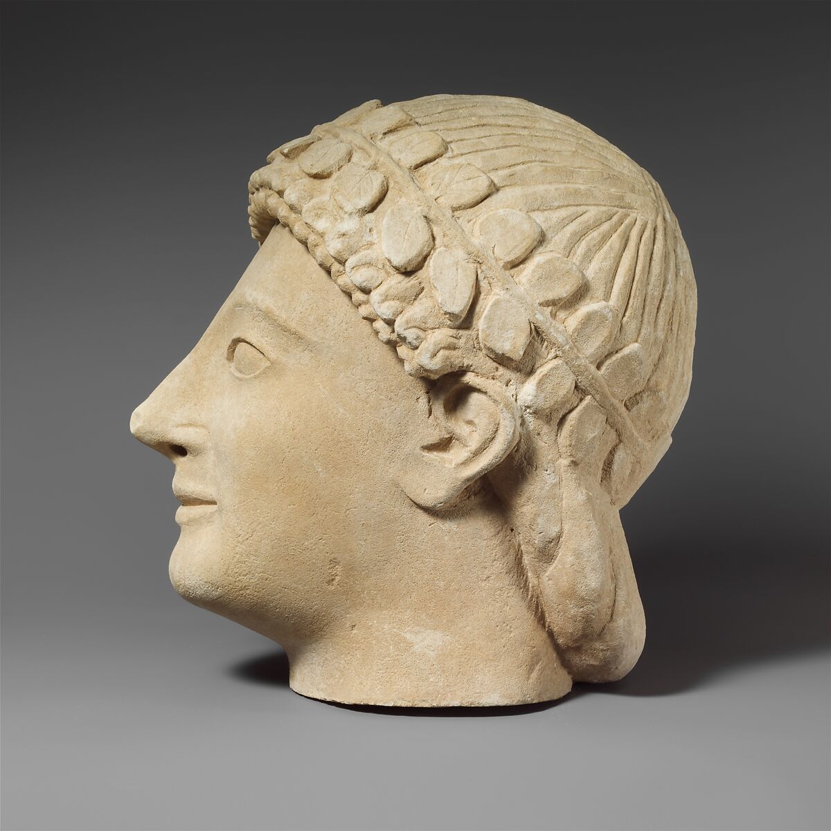 Limestone head of a beardless male votary with a wreath of leaves, Limestone, Cypriot