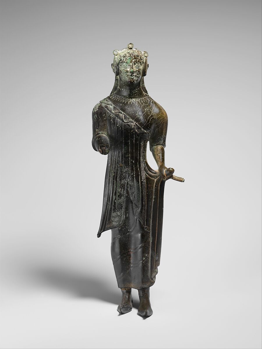 From the description by the Metropolitan Museum of Art: "This statue, perhaps the best-known Etruscan figural bronze in the Museum's collection, was produced at one of the major bronze working centers, probably Vulci or Chiusi. The artist was clearly inspired by archaic Greek korai, votive statues of young women, a connection especially noticeable in the typical frontal pose with right hand extended and left hand holding the garment. However, the sculptor was not especially concerned about the accurate depiction of costume. The Greek himation (cloak), for example, is misrepresented." (MET, 2021).