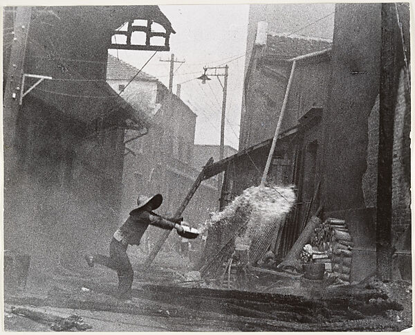After incendiary bombardments, a woman tries futilely to extinguish the fire. Hankow, Robert Capa (American (born Hungary), Budapest 1913–1954 Thai Binh), Gelatin silver print 