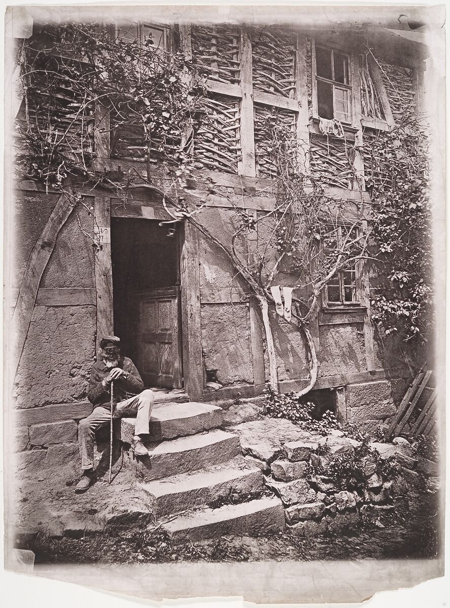 [Man Sitting on Steps of House with Socks Hanging on Nearby Vine to Dry], Unknown (German), Collotype 