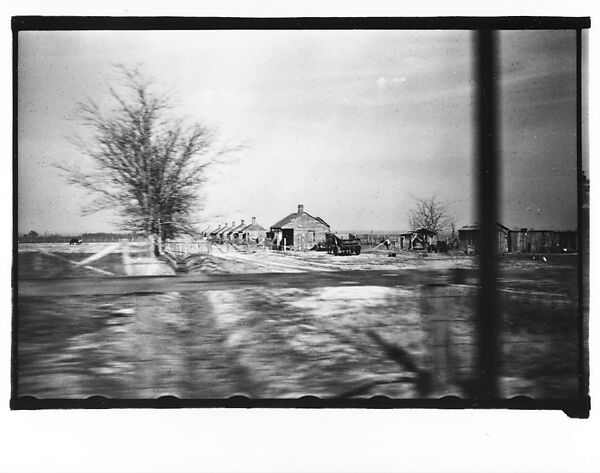 [Row of Wooden Houses with Surrounding Farm Buildings in Field, From Moving Automobile, Louisiana]