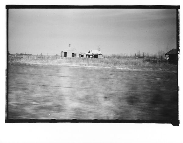 [Wooden House and Adjacent Farm Building in Field, From Moving Automobile, Louisiana]