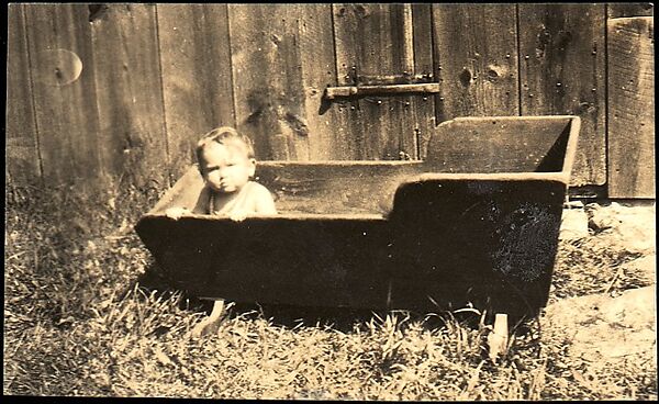 [Anita Skolle, Daughter of Hanns and Elizabeth Skolle, in Wooden Trough Before Barn Façade]