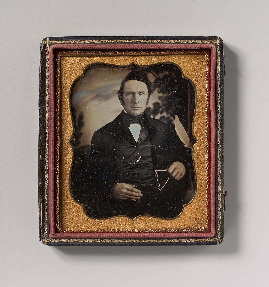 [Man Holding Glasses in Front of Painted Outdoor Backdrop], Unknown (American), Daguerreotype with applied color 