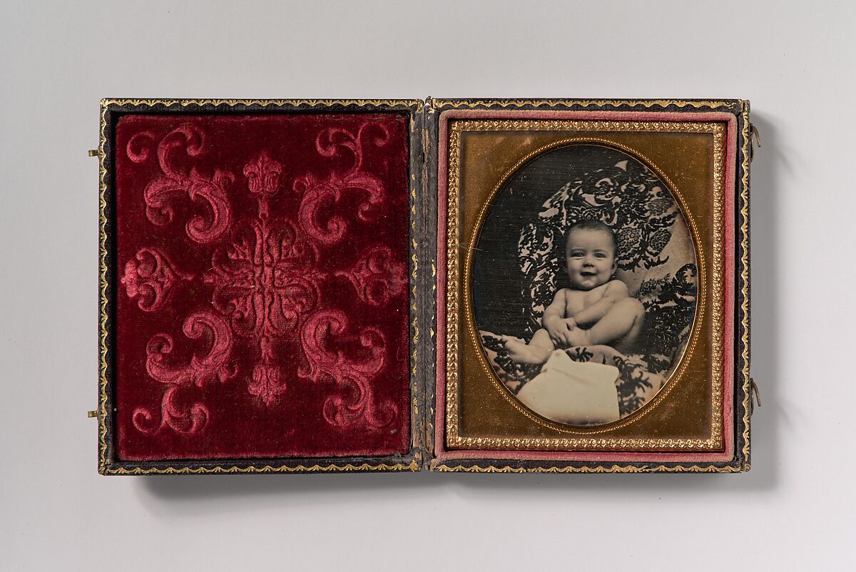 [Smiling, Nude Baby Holding Foot, Seated on Furniture Draped with Floral Print Fabric], Unknown (American), Daguerreotype with applied color 