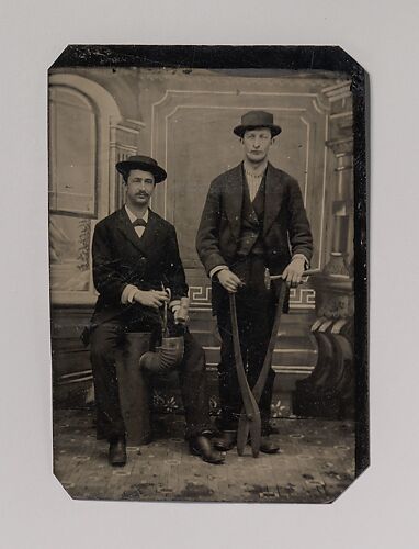 [Two Stovepipe Makers, One with a Hammer and Tin Snips, the Other Sitting on Stovepipe Assembly with Tin Snips and Mallet]