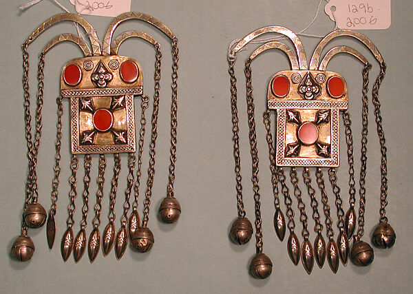Boy's Amulet, One of a Pair, Silver, fire-gilded with gallery wire, stamped bead and applique decoration, rams' heads upper terminations, link chains, bells, embossed pendants and table cut carnelians