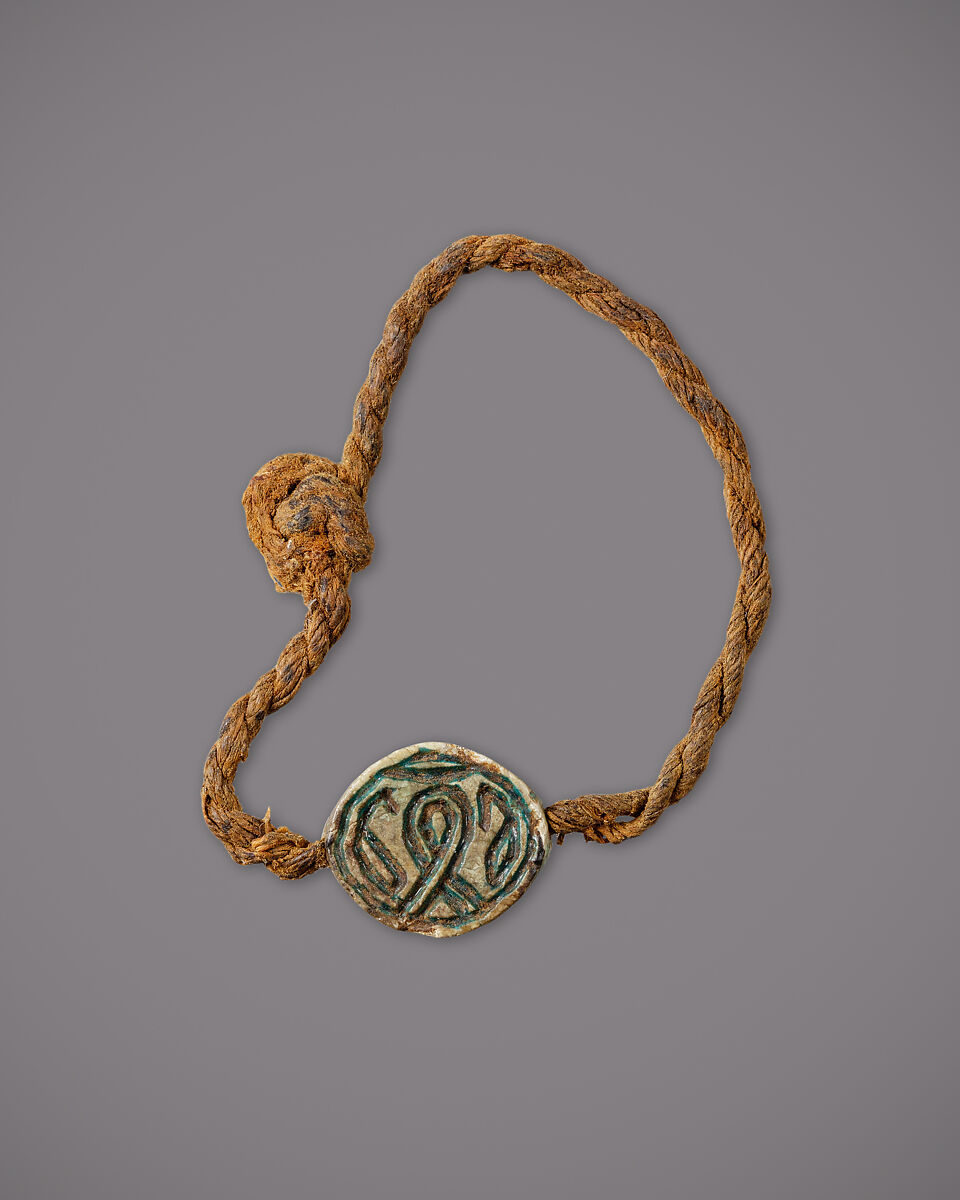 String Bracelet with a Cowroid Amulet, Glazed steatite, linen cord 