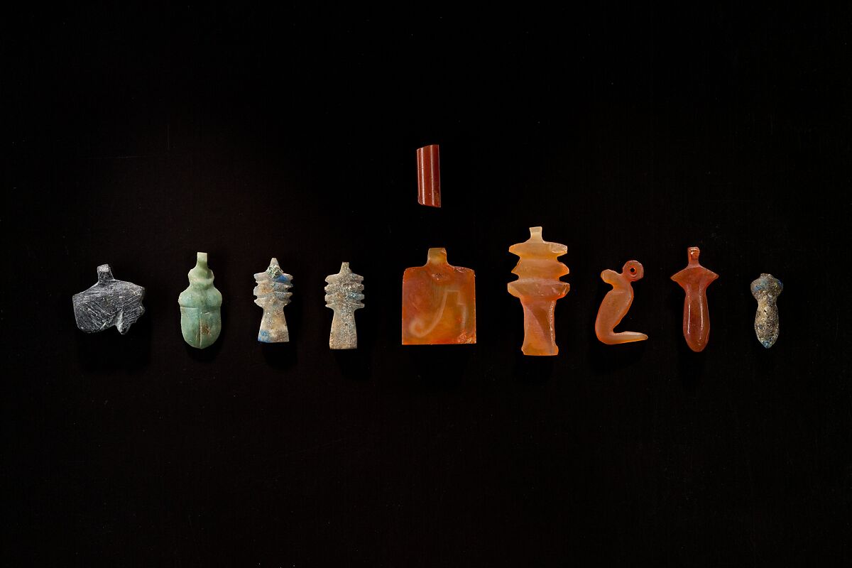 10 Amulets: 1 wedjat, 1 scarab, 3 djed pillars, 1 incised plaque, 1 uraeus, 2 wadj signs, and 1 cylindrical bead, Lapis lazuli, stone, carnelian, glass 