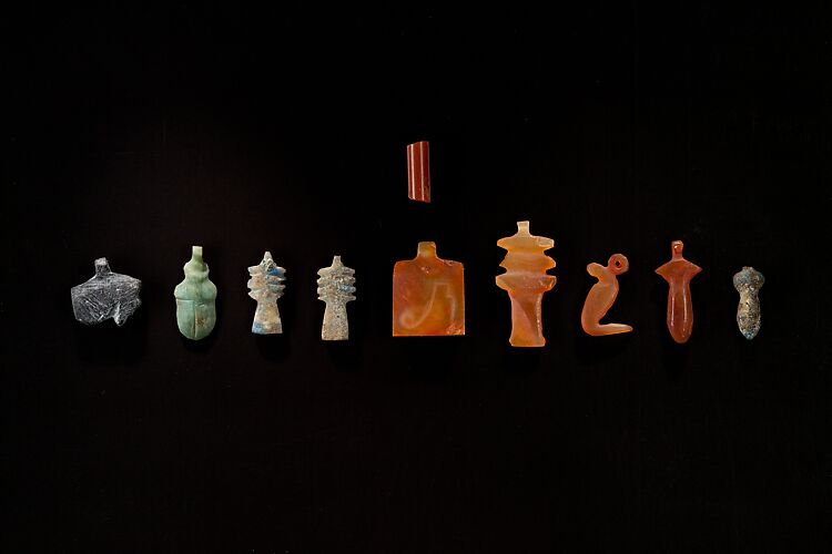 10 Amulets: 1 wedjat, 1 scarab, 3 djed pillars, 1 incised plaque, 1 uraeus, 2 wadj signs, and 1 cylindrical bead