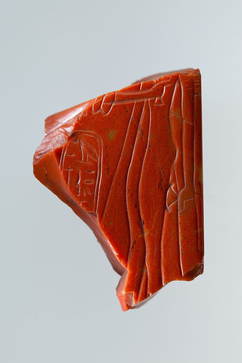 Statue fragment from a standing figure whose back pillar has cartouche of Ramesses II, and the figure of queen Nefertari incised on side, Red Jasper 