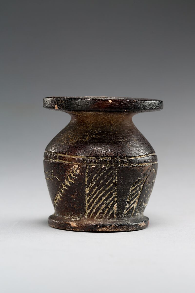 Kohl jar decorated wtih Horus falcon and grotesque figure, Blackened limestone