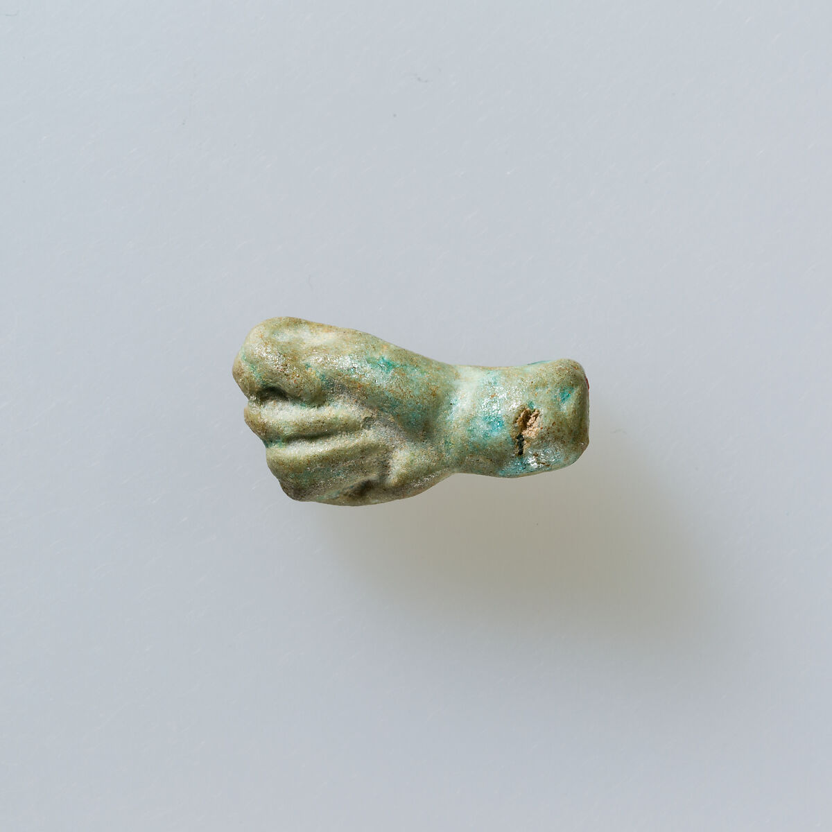 Amulet of fist with thumb thrust between first two fingers, Pale green faience 