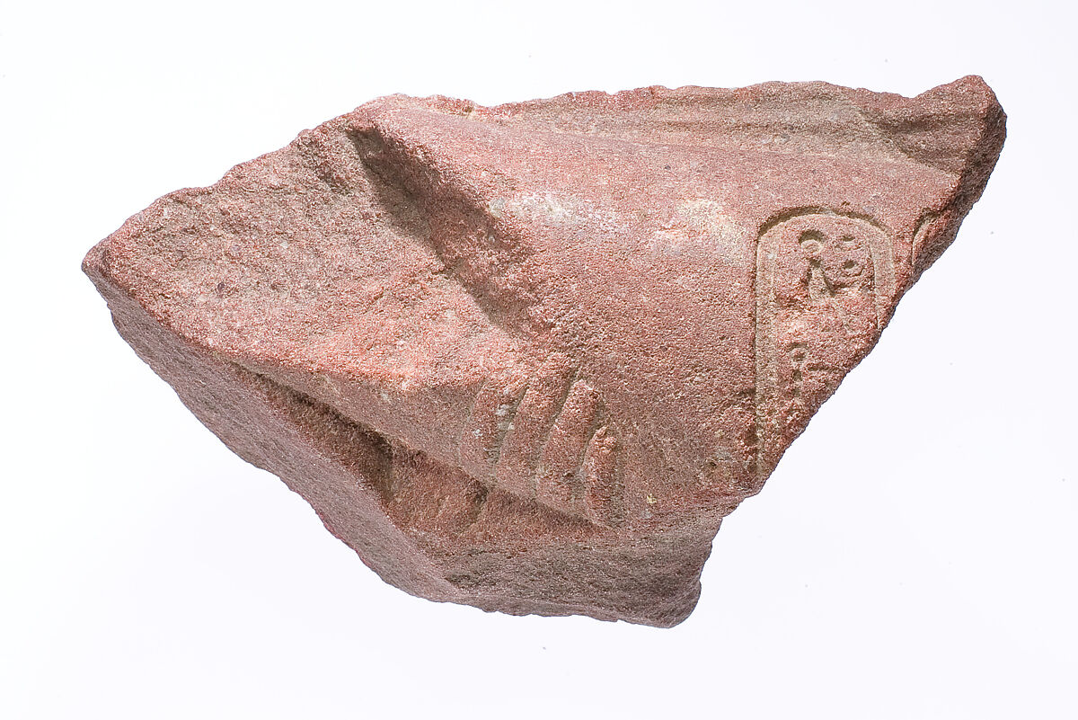 Forearm from a bent royal arm crossing the front profile of figure's body and the rear profile of a second figure, arm marked with Aten cartouches, supported by the hand of an Aten ray, Red quartzite 
