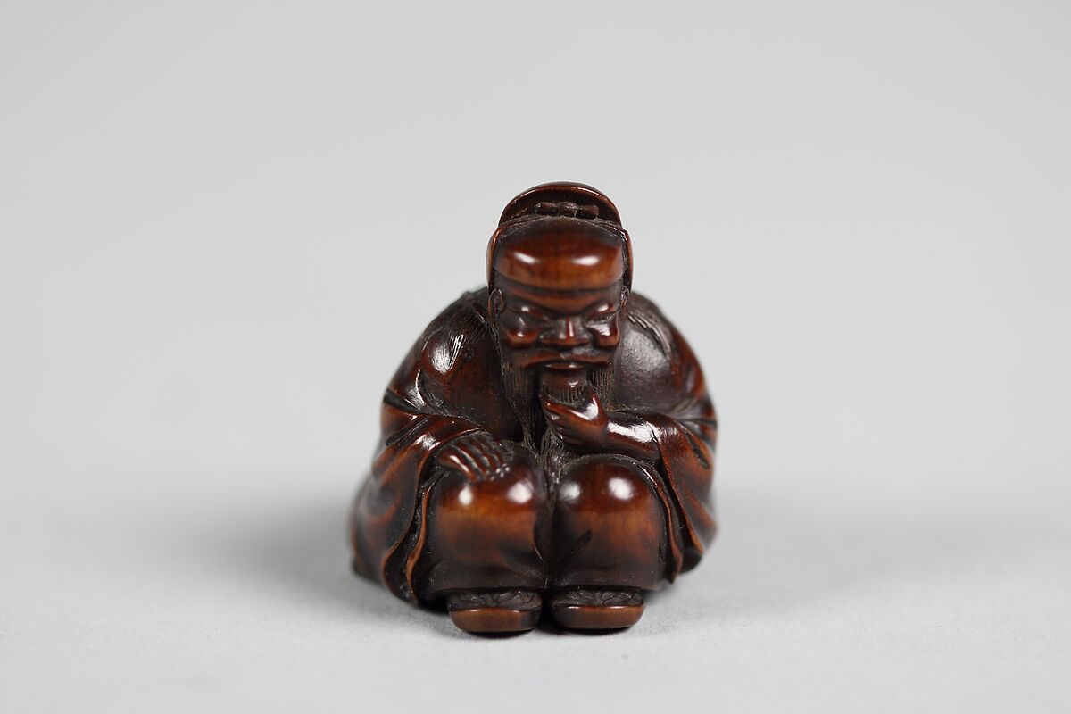 Netsuke of Seated Figure of an Old Man with Backpack Containing a Mask, Wood, Japan 