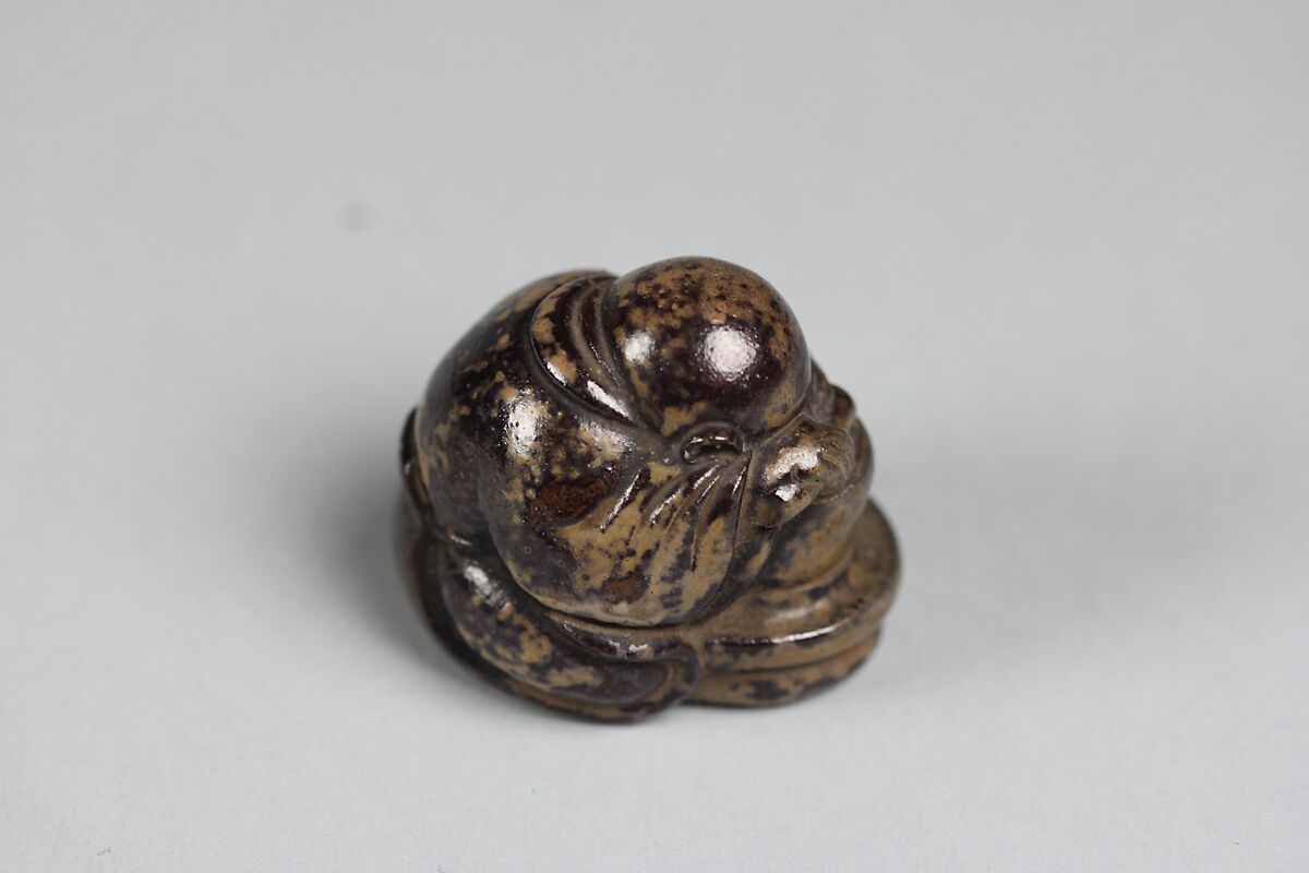 Netsuke of of a Priestling Asleep over a Stonemill, Pottery covered with a mottled black and yellow glaze., Japan
