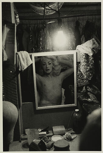 Blonde female impersonator framed in a mirror beneath a light bulb, N.Y.C.