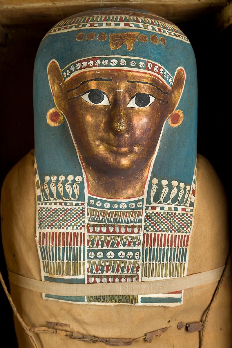 Mummy of Tasheriteniset with mummy mask and other cartonnage elements, also with garland of plants, Mummified human body, linen, mummification material, painted and gilded cartonnage, plant remains