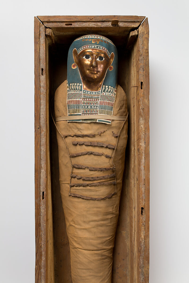 Mummy of Tasheriteniset with mummy mask and other cartonnage elements, also with garland of plants, Mummified human body, linen, mummification material, painted and gilded cartonnage, plant remains