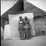 Two Women in Front of a Thatch-Roof House