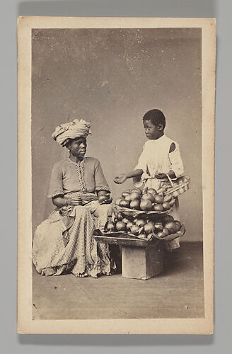 [Studio Portrait: Seated Woman and Standing Boy Street Vendors with Vegetable Baskets, Brazil]